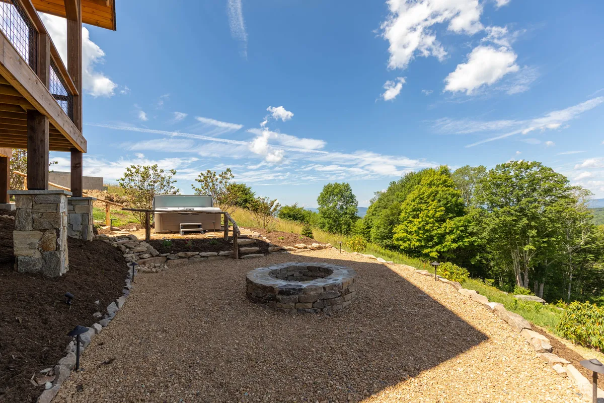 A cozy fire pit anchors an outdoor patio area, complete with a gravel pathway and lush landscaping. The seating arrangement encourages guests to gather for fireside chats, storytelling, or stargazing after a day of adventure.