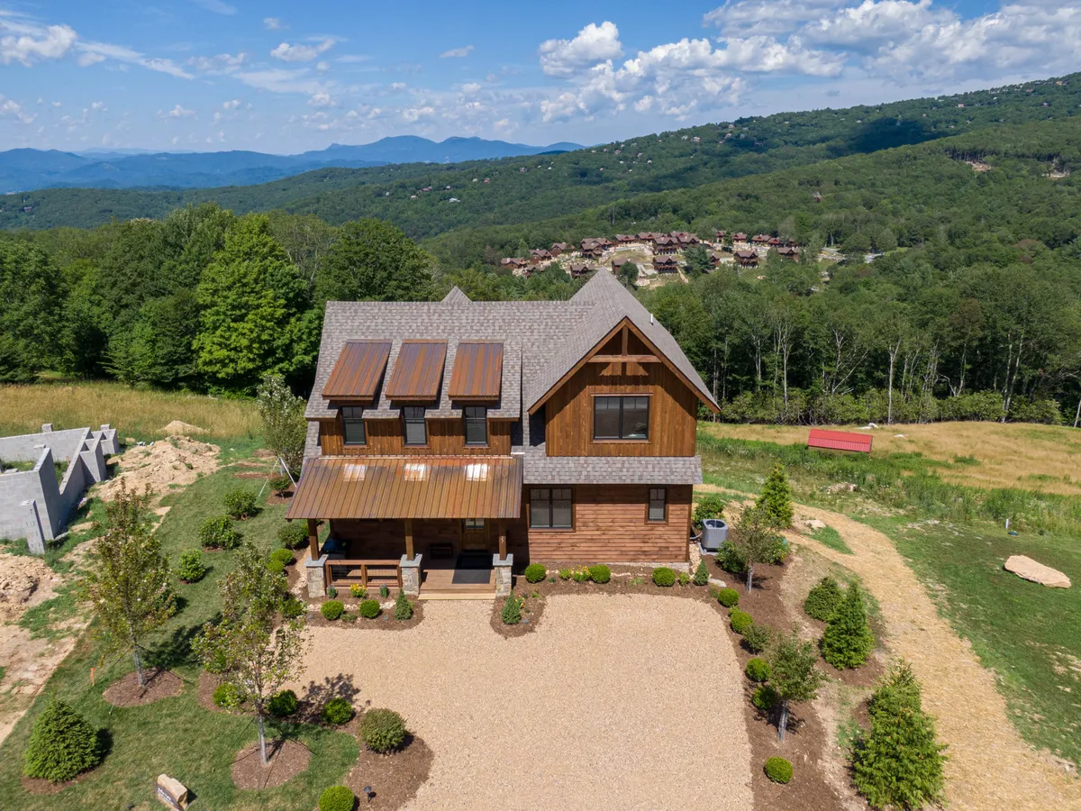 An exterior shot of the house nestled in a tranquil landscape, with the driveway and porch visible. The surrounding greenery and open space hint at access to nature walks directly from the property, while the welcoming porch reinforces the seamless transition between indoor comfort and outdoor adventure.