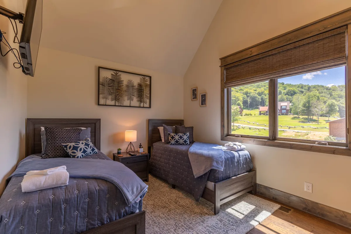 A cozy twin room featuring two twin beds, decorative artwork, a shared nightstand with a lamp, and a window offering natural light and views. The layout invites togetherness while ensuring personal space.