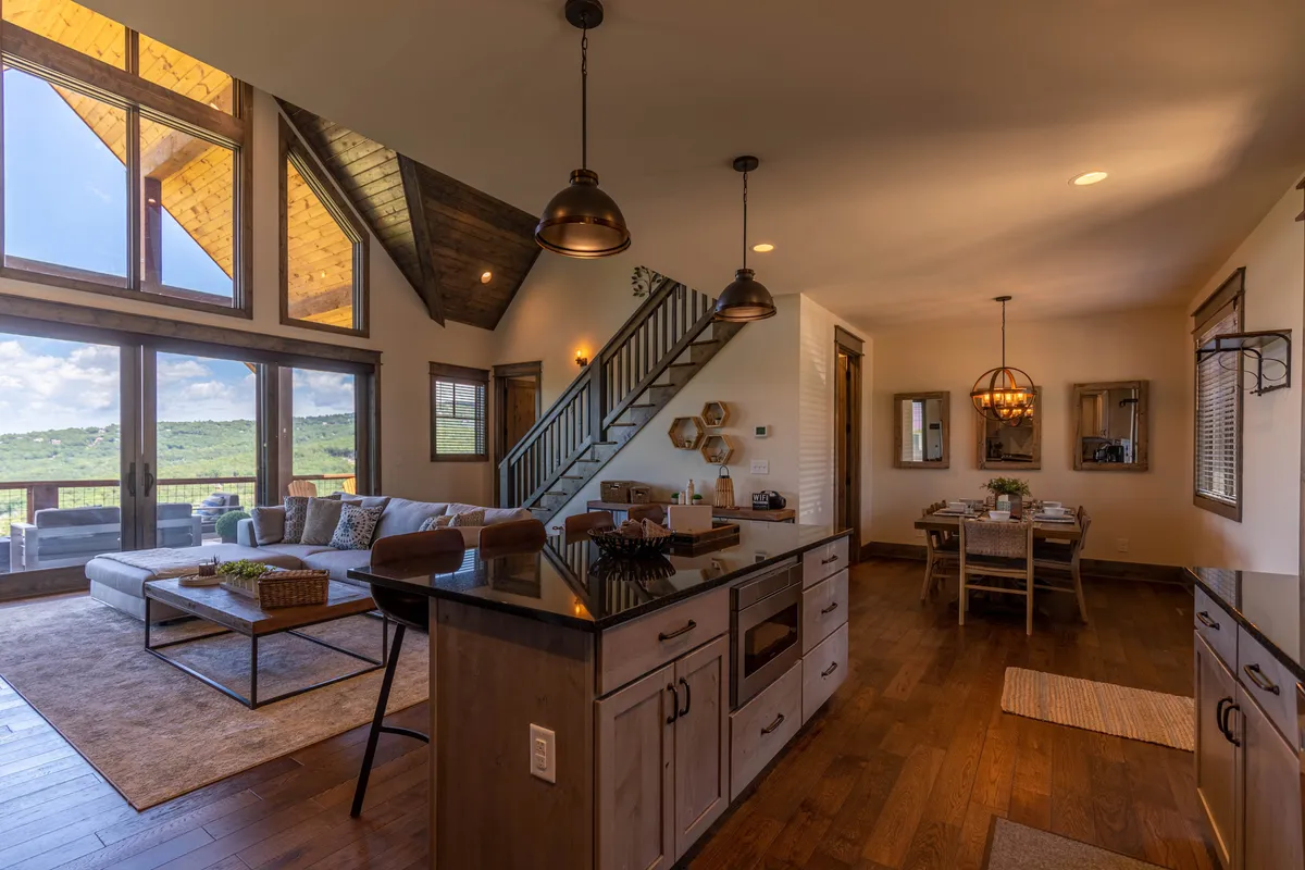 A bright, open-plan living space featuring a modern kitchen island, cozy seating area, and a dining table set for meals. Large windows frame beautiful mountain views, filling the room with natural light. The layout encourages interaction, relaxation, and enjoyment of the scenic surroundings.