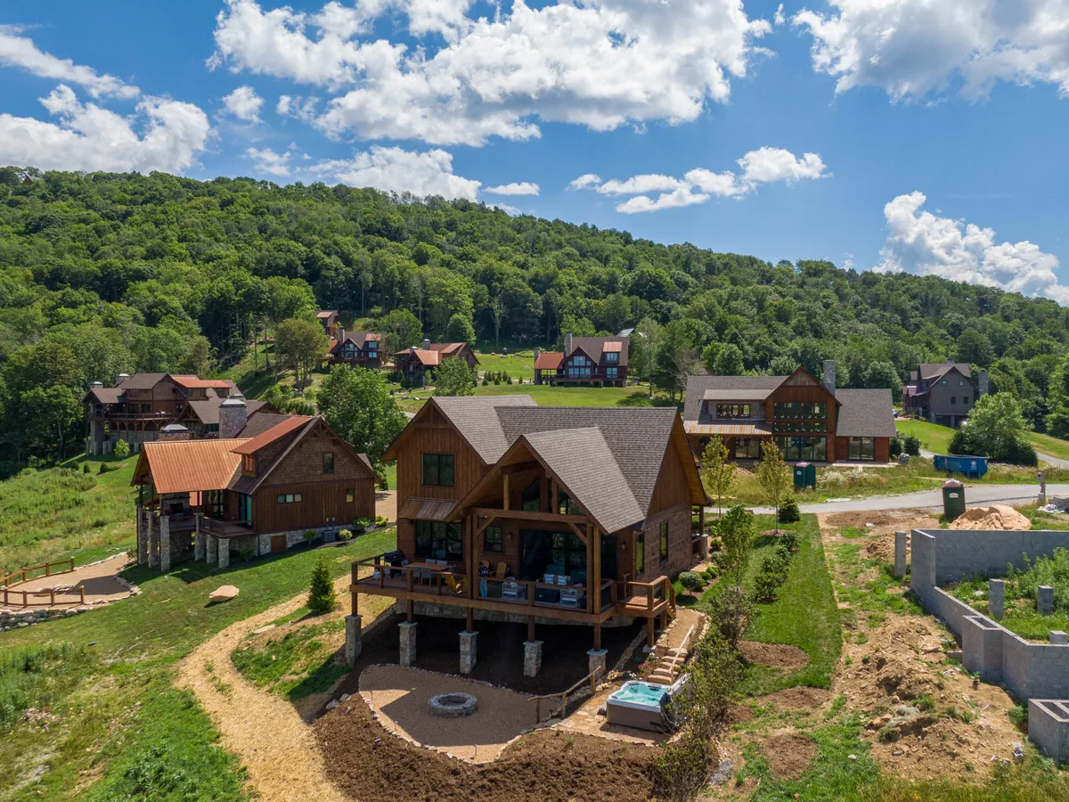 This image highlights the modern cabin's exterior surrounded by lush greenery, with a visible outdoor seating area set within a serene environment. Neighboring homes are subtly visible, emphasizing the community's safe, welcoming setting. The space feels ideal for family gatherings, barbecues, and making memories.