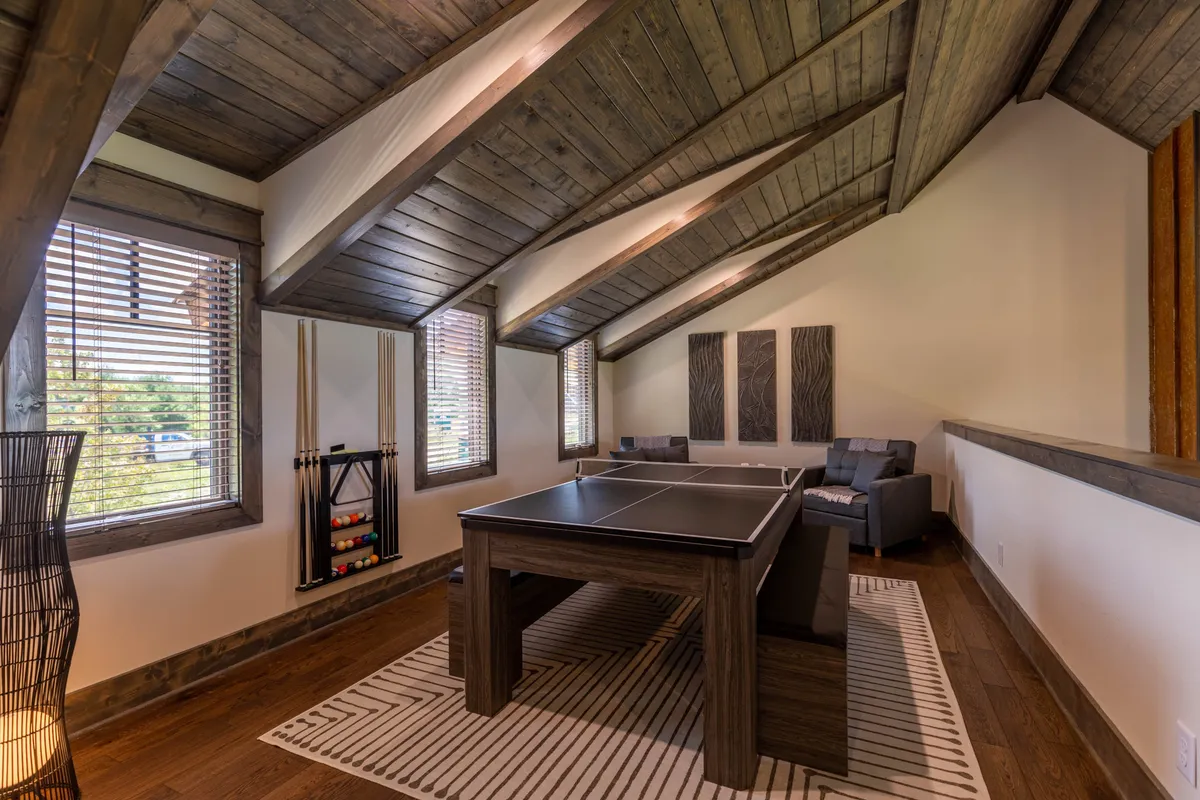 A loft area with a pool table, comfortable seating, wooden beams, and large windows. The space feels open and inviting, perfect for both late-night games and extra sleeping arrangements.