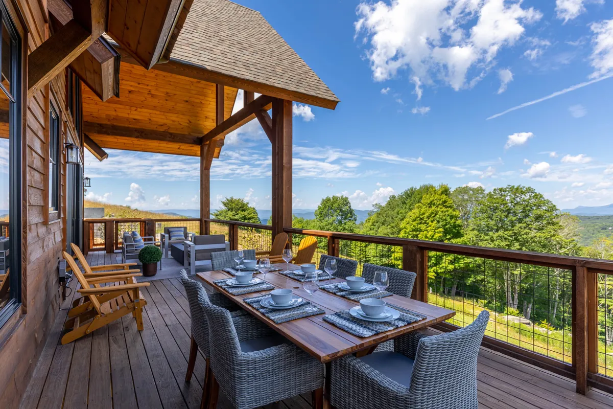 A beautifully arranged outdoor dining table sits atop a spacious deck, surrounded by comfortable seating and offering sweeping views of the surrounding landscape. The setting sun casts a golden hue, creating an inviting space for group meals, celebrations, or relaxed evenings under the stars.