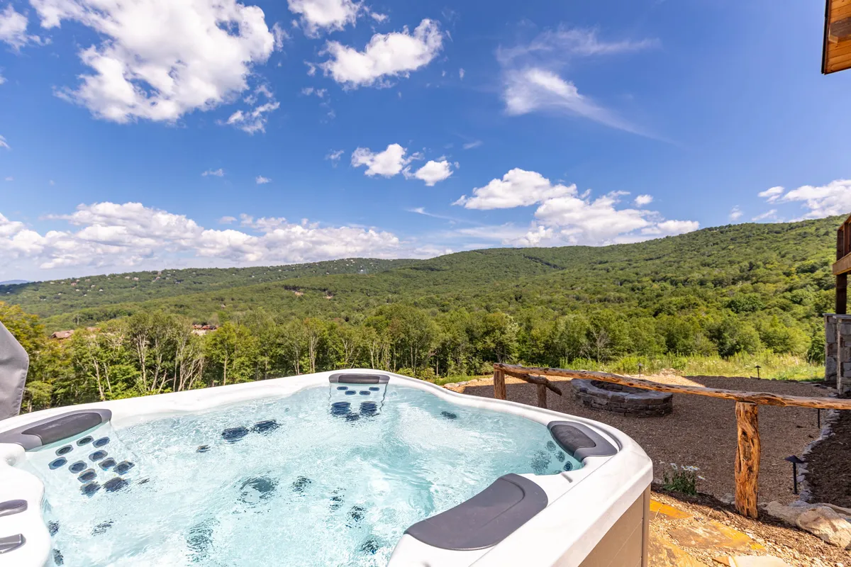 A tranquil hot tub set on an outdoor deck with sweeping mountain views beneath a sky dotted with clouds. The scene evokes relaxation, with the hot tub inviting guests to unwind while taking in the natural majesty that Bella Vista offers.