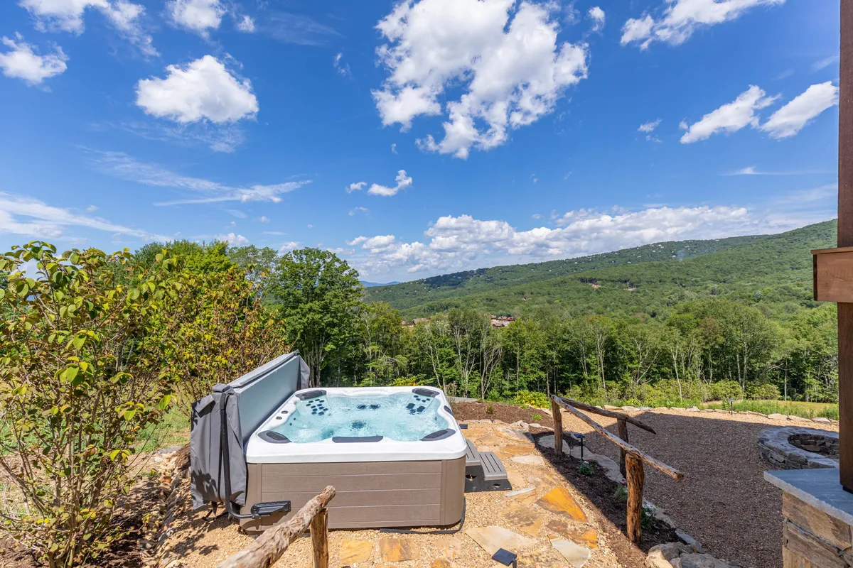 This image features a luxurious hot tub set outdoors, surrounded by lush landscaping with expansive mountain views. The sky overhead hints at a serene environment, ideal for unwinding and gathering together. The setting seamlessly connects guests to nature while offering a space for relaxation and celebration.