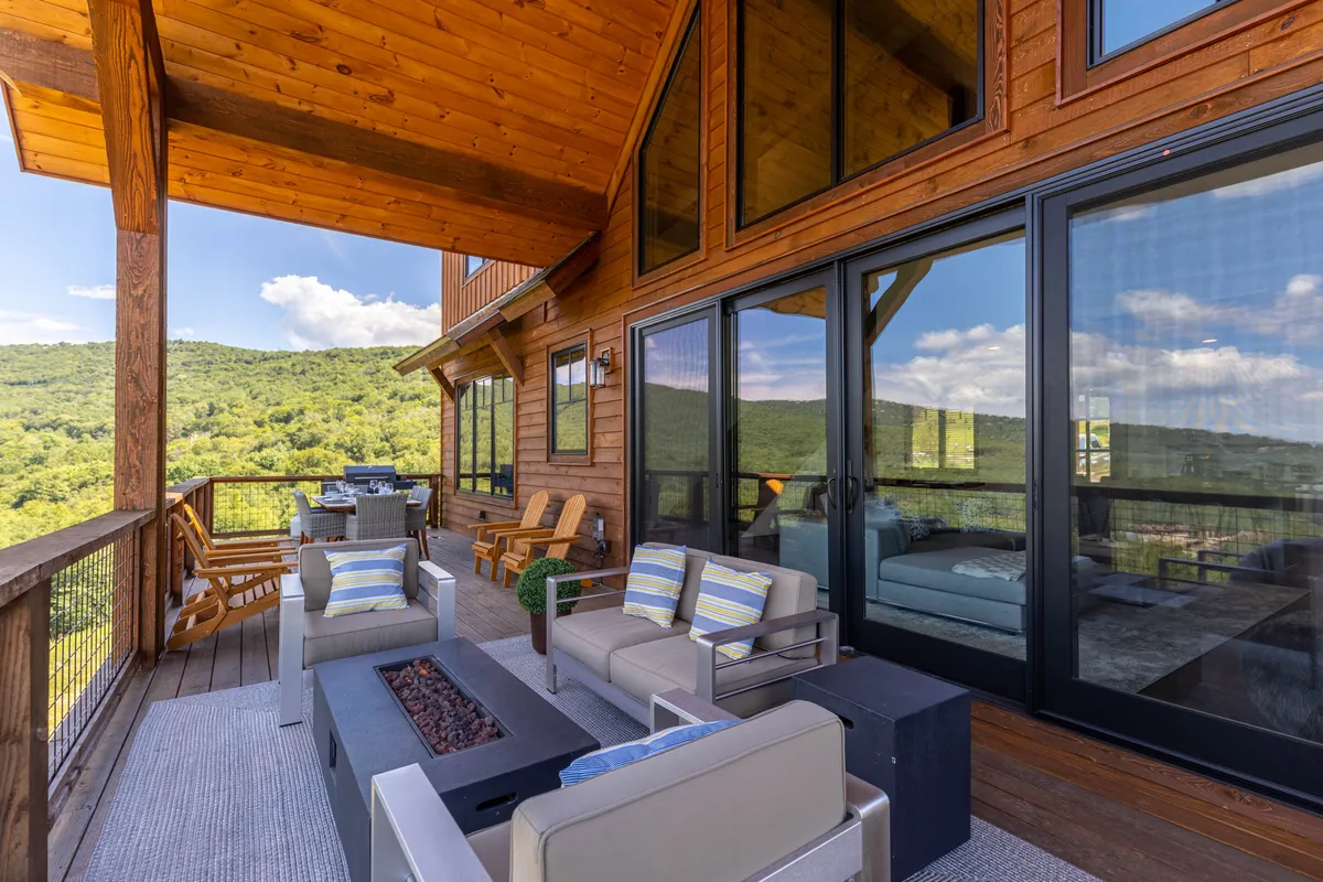 This exterior image showcases a welcoming outdoor seating area arranged around a fire pit, with expansive mountain views visible beyond the large windows of the house. The space feels inviting and designed for gatherings, with comfortable seating perfect for families to relax after a day of adventure. The setting sun and the relaxed mood suggest memorable evenings spent outdoors.