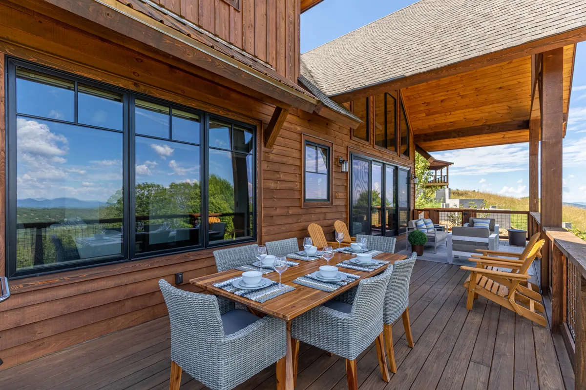 A beautifully set outdoor dining table sits beside a comfortable lounge area, all framed by large windows and breathtaking mountain scenery. The space is designed for social gatherings, shared meals, and relaxed conversation with friends and family, offering both intimacy and openness to nature.