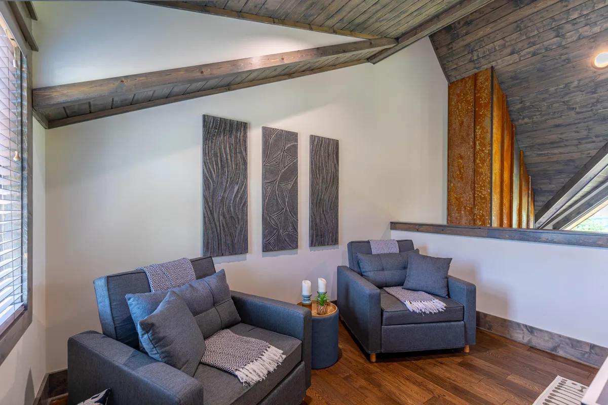 A cozy nook with two comfortable armchairs adorned with soft cushions, set against a backdrop of abstract wall art and natural wood accents. The intimate setting suggests a peaceful spot for reading, conversation, or quiet relaxation, embodying a tranquil part of the multifunctional loft space.