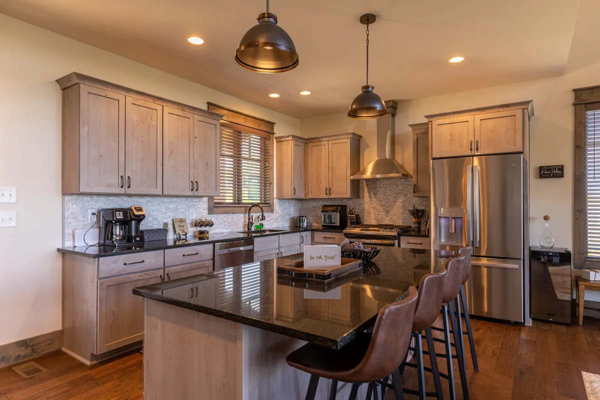 A modern kitchen highlighted by a generous island, stainless steel appliances, wooden cabinetry, and pendant lighting. The space feels warm and functional, with room for guests to gather, cook, and converse. The kitchen is well-equipped for entertaining, with ample countertop space and a welcoming layout.