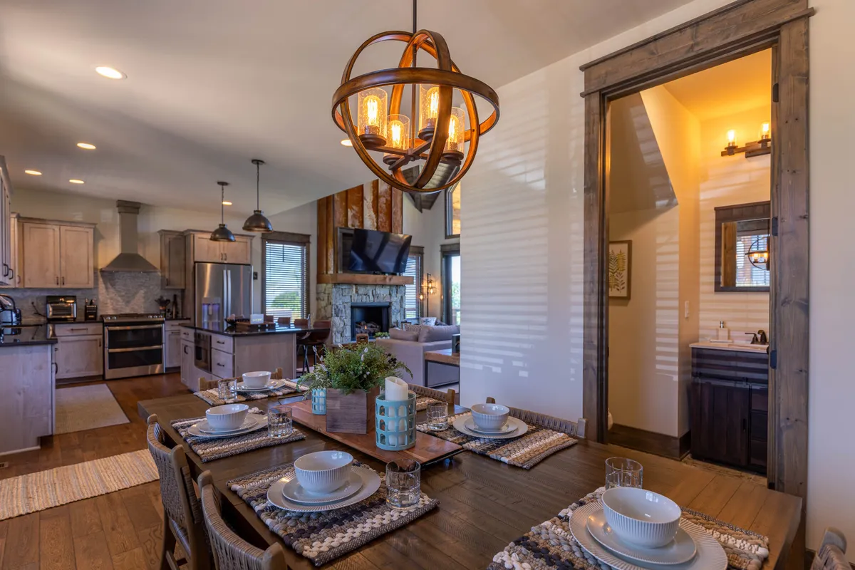A cozy dining area set for a meal, adorned with a chandelier above and a fireplace nearby. The dining table is ready for guests, and the adjacent kitchen area is visible, creating a seamless connection for entertaining and family meals. The inviting atmosphere is perfect for shared moments and celebrations.