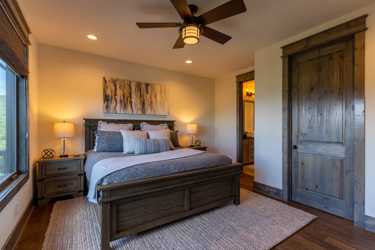 A beautifully styled king bedroom with a plush bed adorned with decorative pillows, wooden bedside tables, and artwork above the bed. Soft natural light pours in through a window, highlighting the calm and inviting aesthetic.