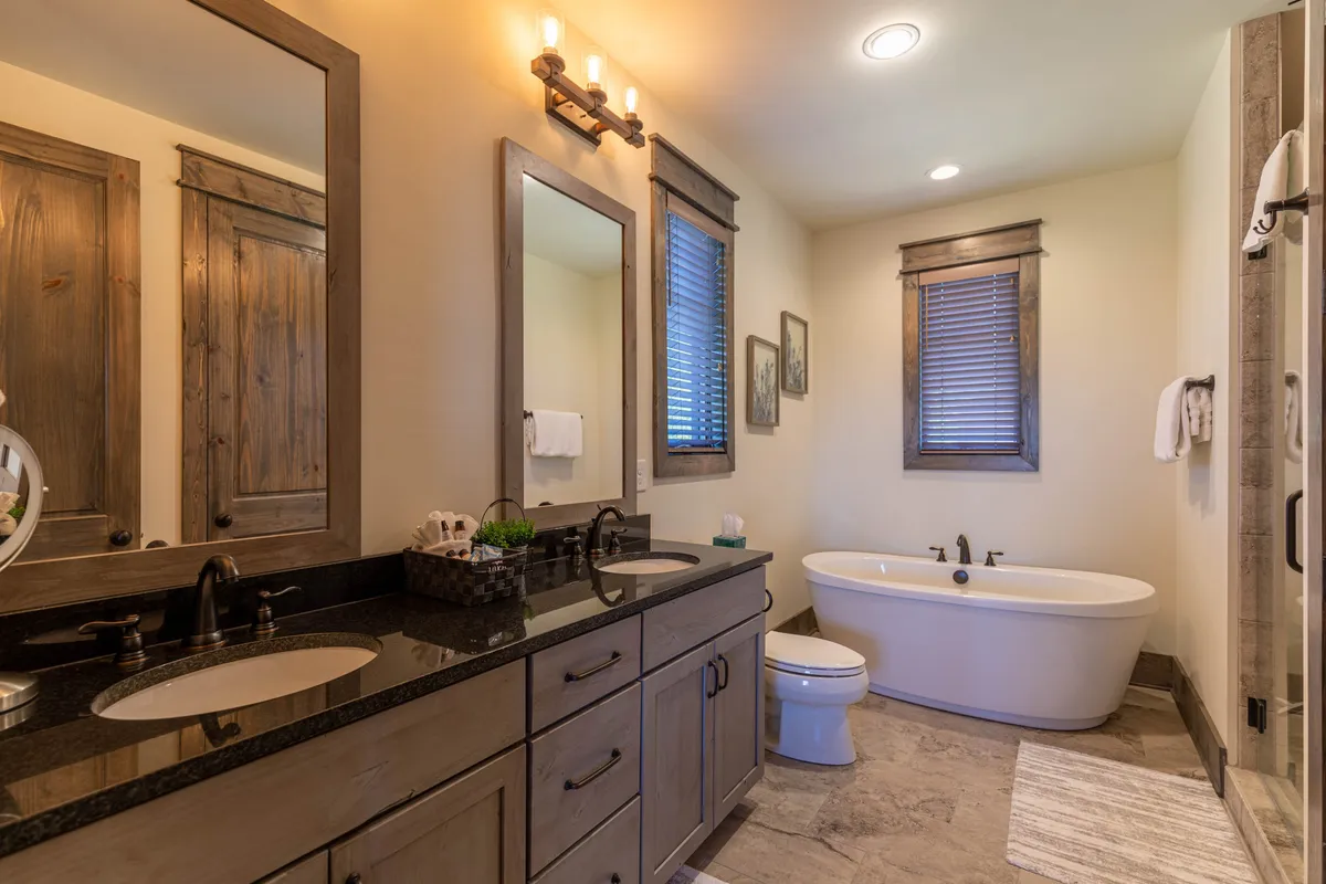A luxurious bathroom with a freestanding soaking tub, double vanity with dual sinks, large mirrors, and a window with wooden shutters. The elegant details create a spa-like ambiance.